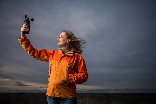 A teacher stands with a camera in a field